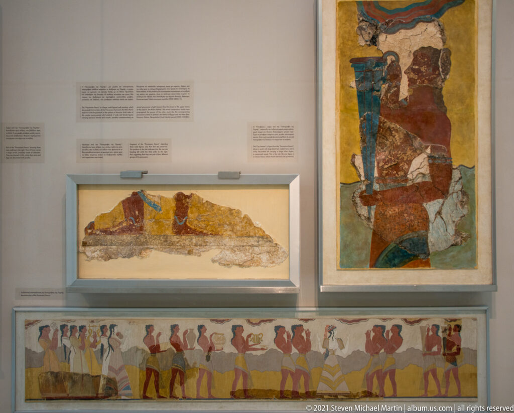 Gallery wall with three Minoan fresco displays, including a tall seated figure and a long procession scene.