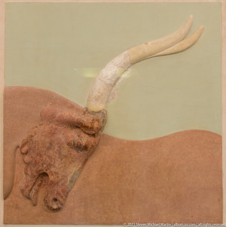 Fragmentary Minoan bull fresco showing a reddish bull head with eye, muzzle, ear, and long pale restored horns.