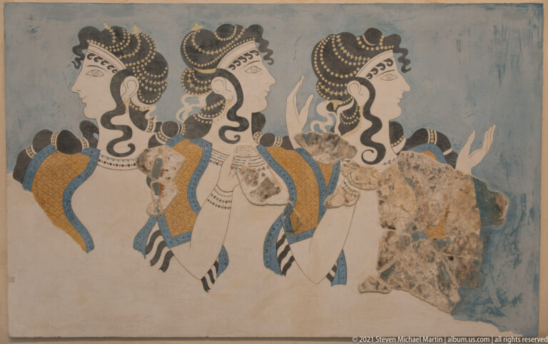 Reconstructed Ladies in Blue Minoan fresco with three profile women wearing elaborate curls, jewelry, and colorful garments.