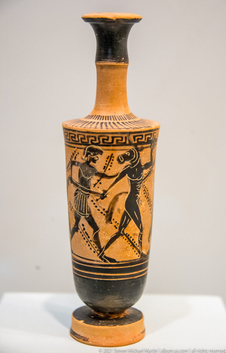 Attic black-figure lekythos with narrow neck, flaring mouth, meander border, and a painted combat scene.