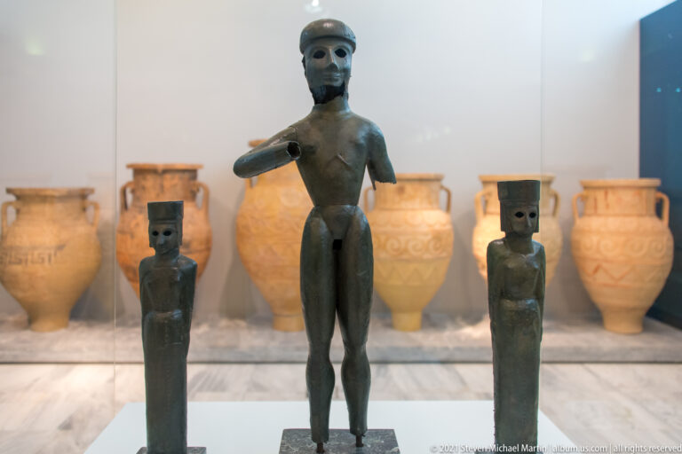 Three standing bronze male figurines, with one taller naturalistic figure between two smaller schematic figures.