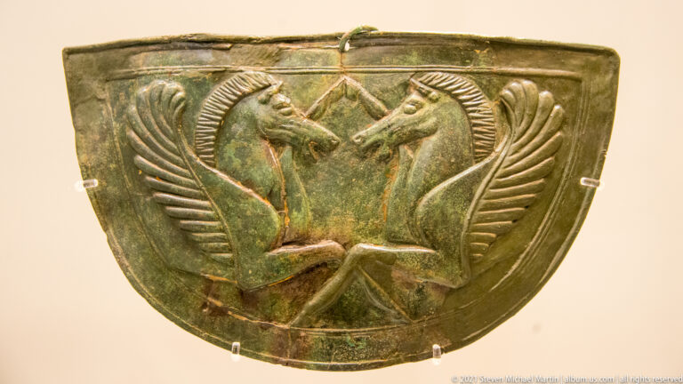 Curved patinated bronze panel with two symmetrical winged horse-like creatures facing one another in relief.