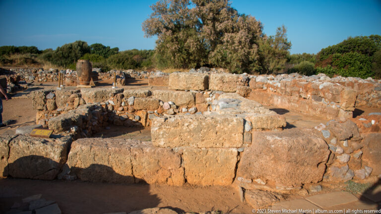 Large rectangular stone blocks forming a substantial wall line, with lower ruins and trees behind.