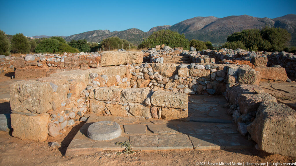Narrow stone-paved passage between thick palace walls with a circular stone base near the foreground.