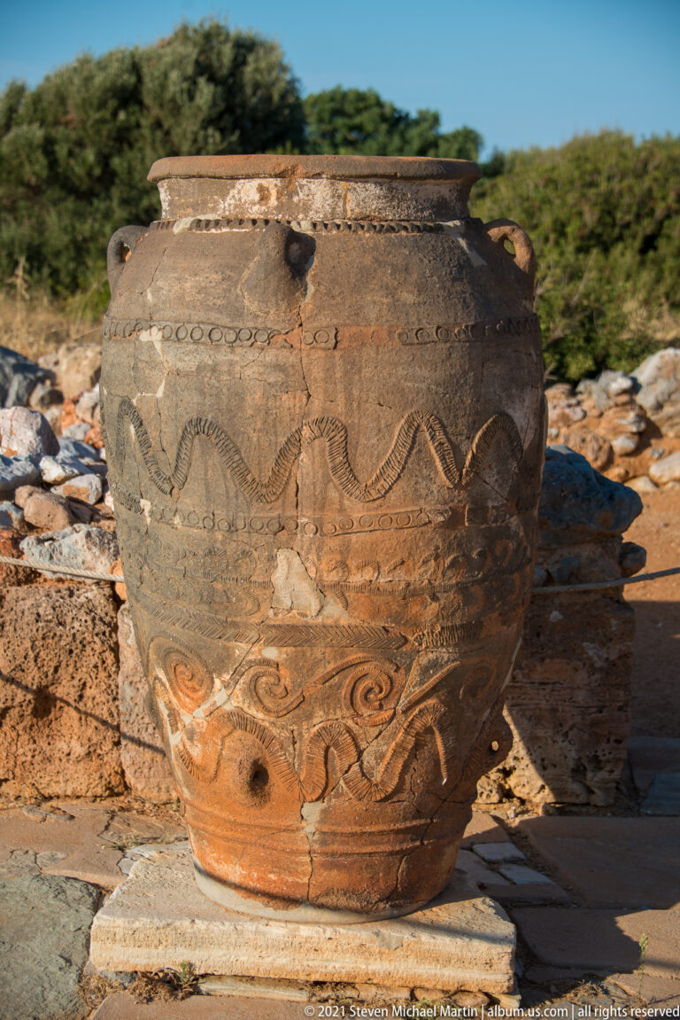 Large decorated ceramic pithos with relief bands, looped motifs, and visible repaired breaks.