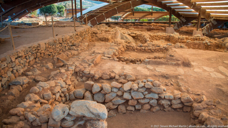 Elevated view of overlapping low stone walls and room foundations beneath the protective shelter.