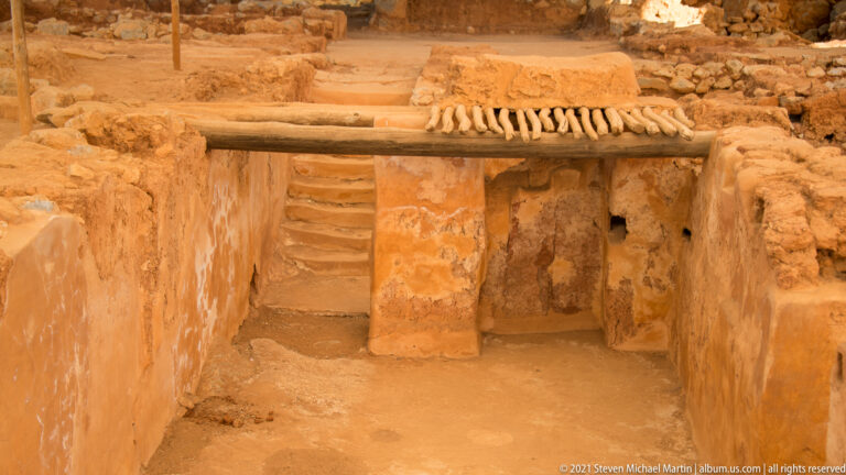 Parallel cylindrical elements bridge a narrow recessed space with steps descending behind them.