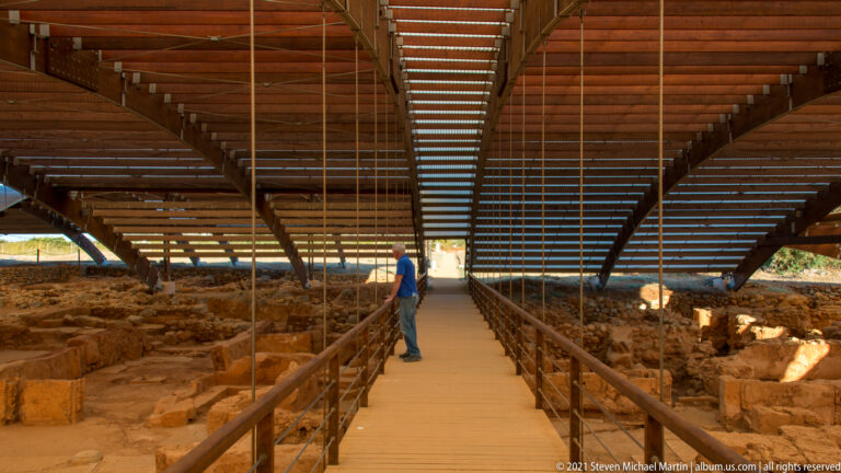 Raised visitor walkway with handrails running through a large roofed excavation, with one person standing midway.