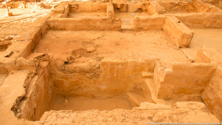 Small rectangular excavated rooms with low walls, light-colored surfaces, and narrow connecting openings.