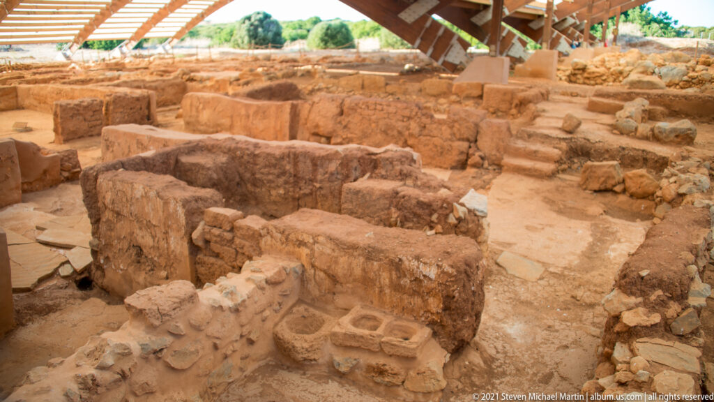 Low excavated walls and small rooms beneath a protective roof at Malia Minoan Palace.