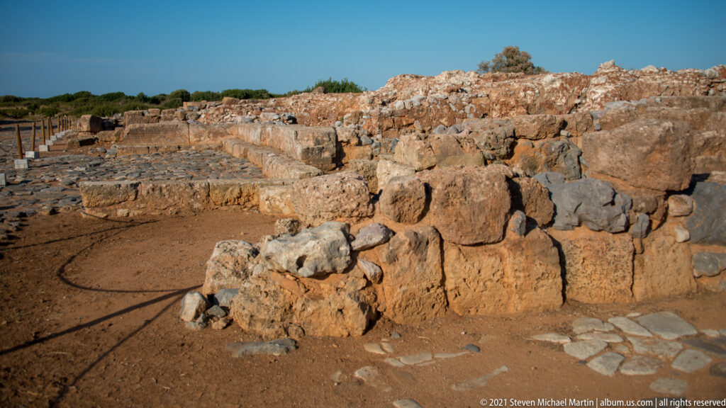 Large squared stone blocks in the foreground with lower rubble walls extending across the Malia ruins.