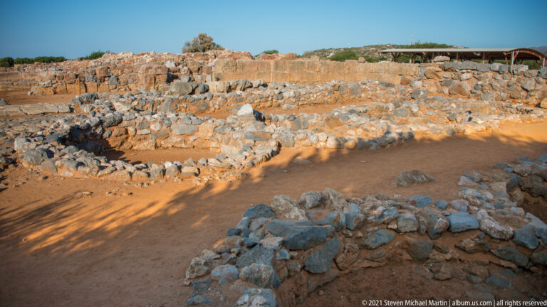 Low stone walls outlining several excavated rooms and passages at Malia in warm sunlight.