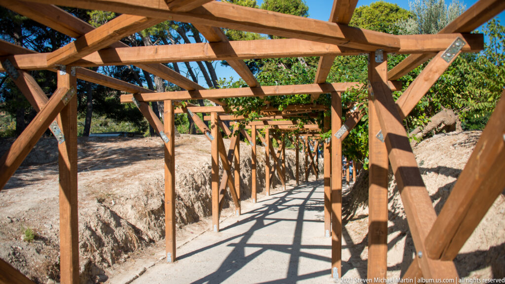 Timber-framed visitor walkway crossing excavated ground at the Palace of Knossos, with repeating beams and strong shadows.