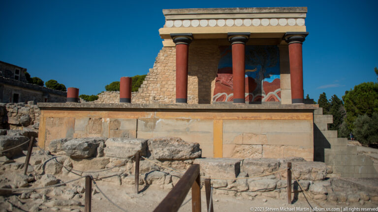 Frontal view of the North Entrance reconstruction with red columns and the bull fresco above rough excavated stonework.
