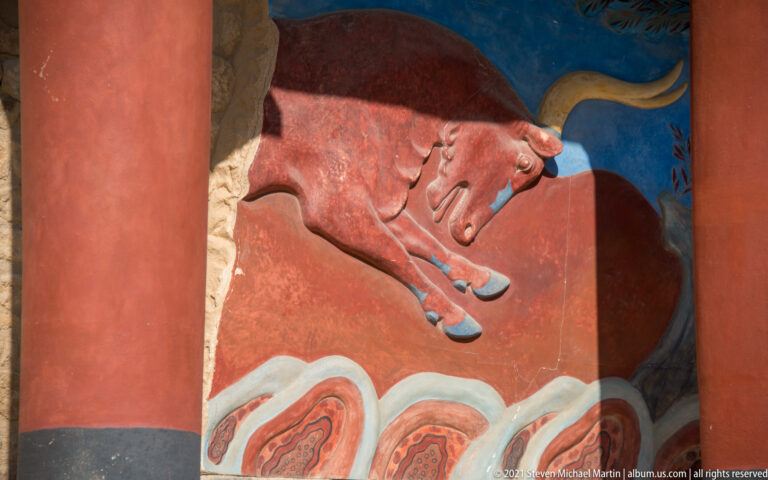 Close detail of a charging red bull with pale horns and extended legs against the blue field of the North Entrance fresco.