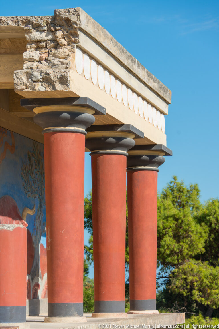 Three reconstructed red Minoan columns with dark capitals beneath a pale entablature at the North Entrance.