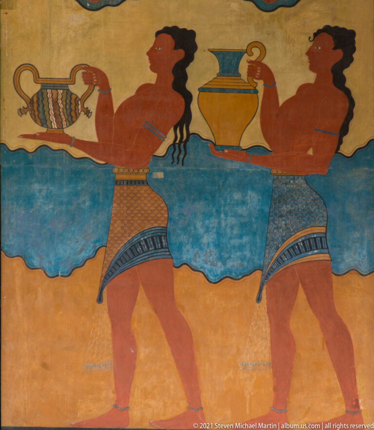 Two profile male figures in a reconstructed Minoan procession fresco carrying decorated vessels against blue and ochre bands.