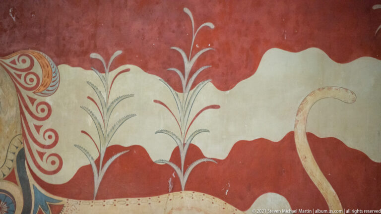 Stylized painted plants on red and pale fields with part of a griffin tail and spotted body at the right edge.
