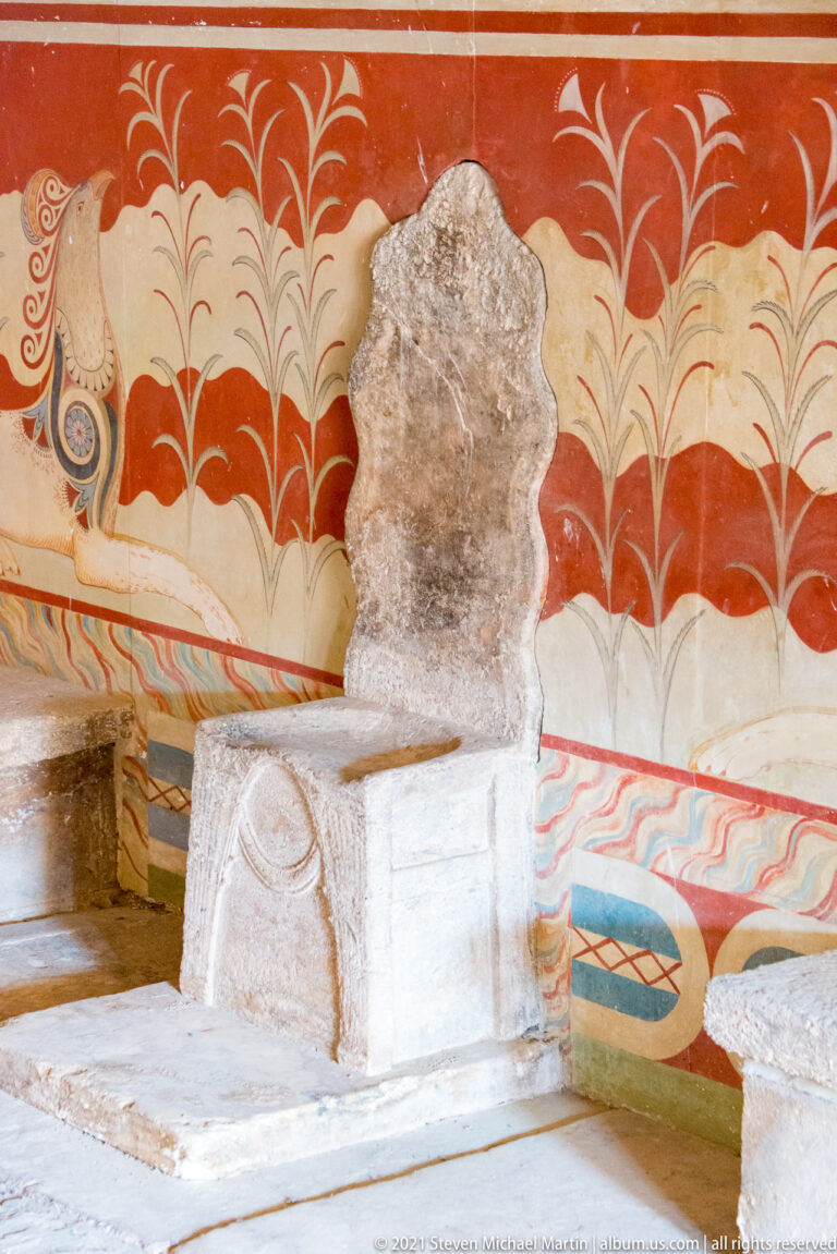 Pale carved stone seat in front of brightly restored red, cream, blue, and turquoise fresco decoration.