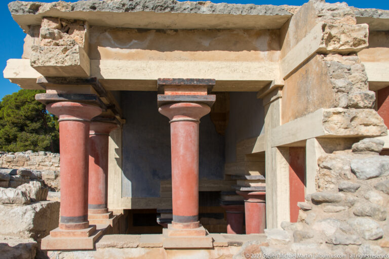 Red reconstructed Minoan columns and pale lintels framing the sunken North Lustral Basin at Knossos.