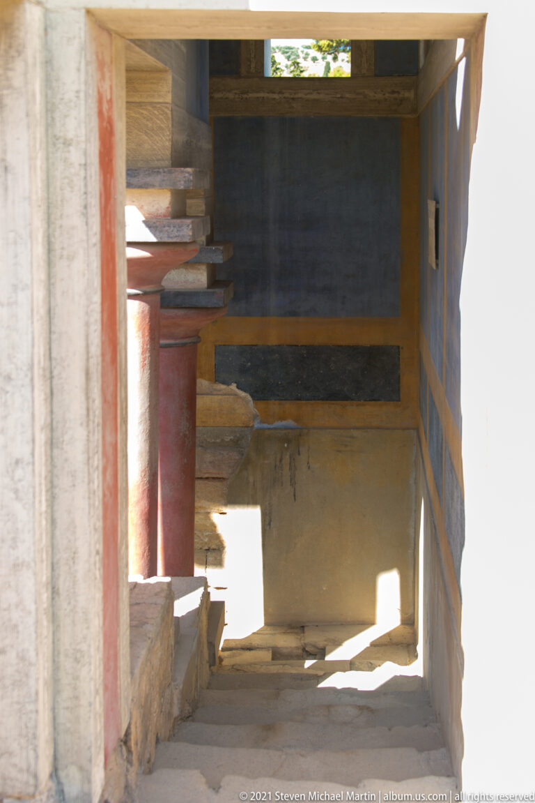 Interior view into the North Lustral Basin with red columns, pale walls, steps, and deep shadow.