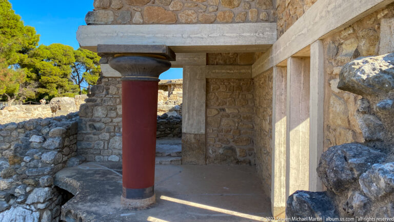 Single red tapered column beneath a restored lintel, surrounded by rough stone walls and pale structural bands.