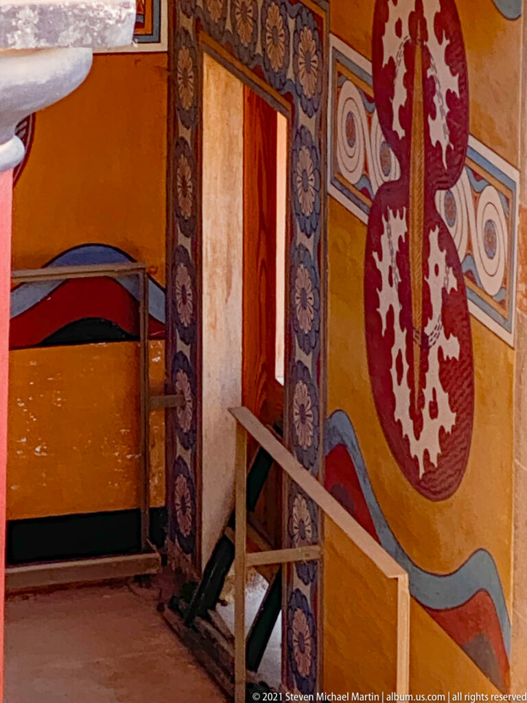 Large red figure-eight shield motif beside an ornately painted doorway with floral and geometric borders.