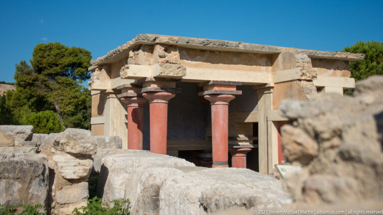 Exterior view of the North Lustral Basin with red columns, pale lintels, and surrounding ancient stone walls.