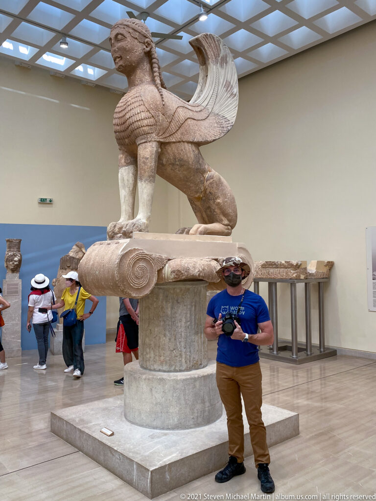 Monumental marble Sphinx of Naxos with human head, lion body, and raised wings above an Ionic capital in the museum.