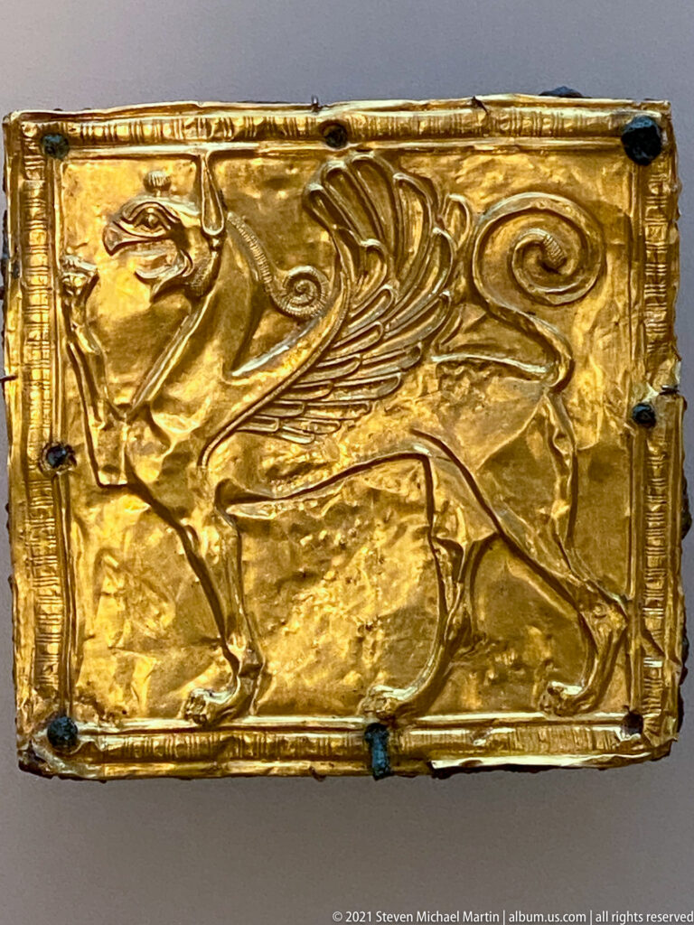 Rectangular gold plaque embossed with a winged quadruped in profile, framed by a narrow raised border.