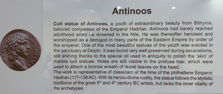 Interpretive panel titled “Antinoos,” with text about his Delphi cult statue and a coin portrait at left.