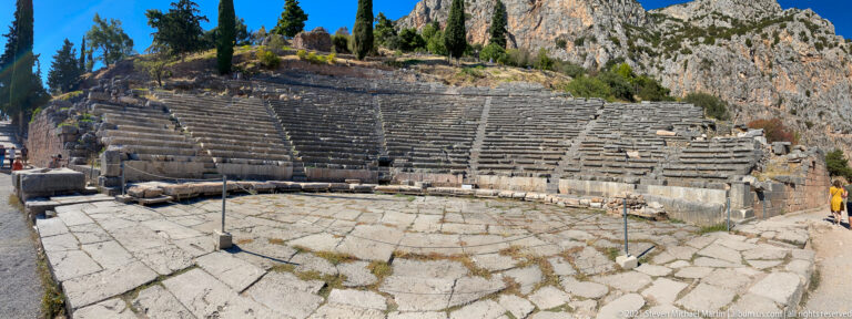 Stone-paved orchestra before curved tiers of seating and stairways in the ancient Theatre of Delphi.