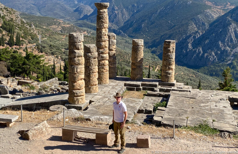 Visitor standing on the Temple of Apollo terrace before six Doric columns and the mountain valley beyond.
