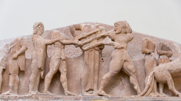 Close view of fragmentary Archaic marble relief with standing male figures in the Siphnian Treasury display.