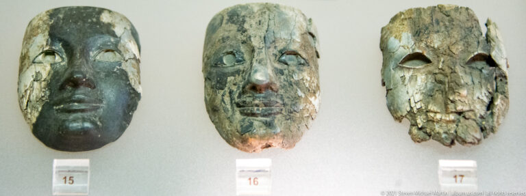 Three small ancient human face plaques or masks displayed side by side, with cracked and fragmentary surfaces.
