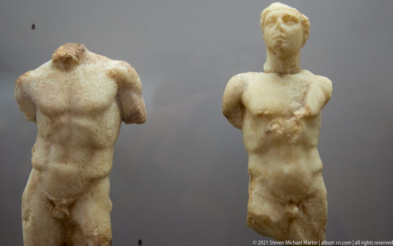 Two fragmentary marble nude male statues displayed side by side, one headless and one retaining its head.
