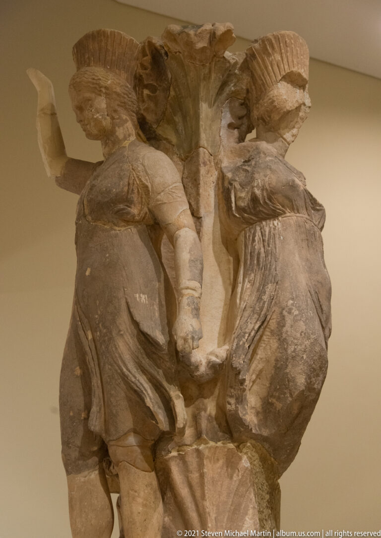 Fragmentary stone sculptural group with a central nude child or youth between larger draped figures.