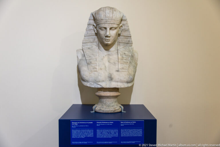 Frontal marble female bust with a broad vertically striped headdress descending beside the face.