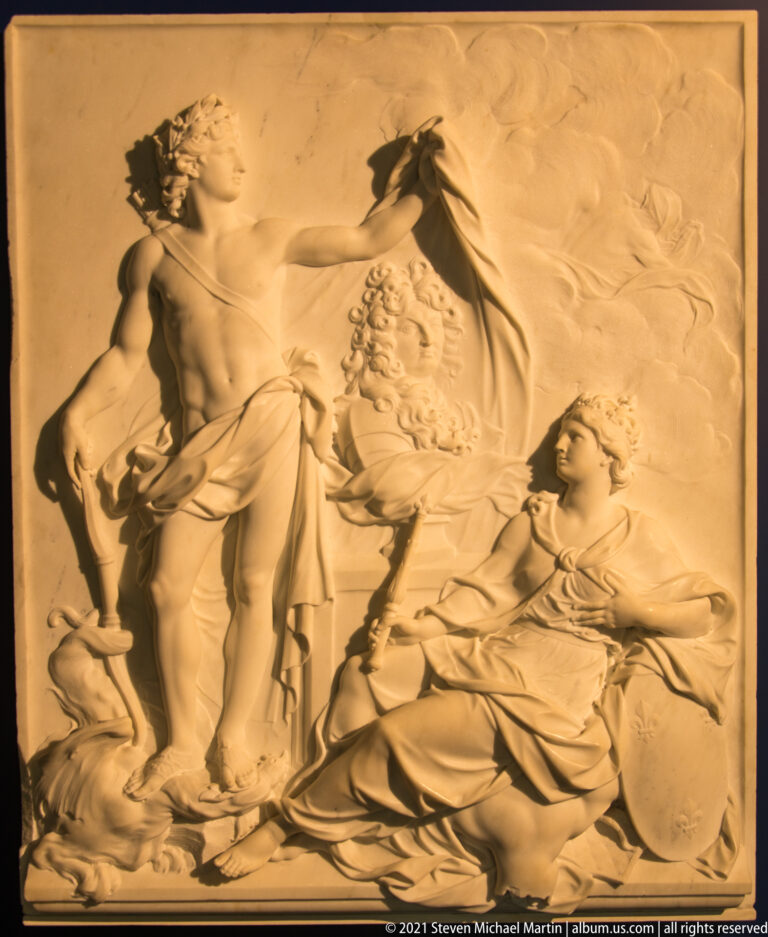 Warm-lit rectangular relief with several mythological figures, including a standing man and reclining woman.