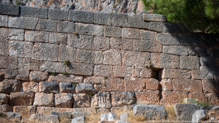 Close view of an ancient block masonry wall with a small rectangular opening and irregular lower courses.