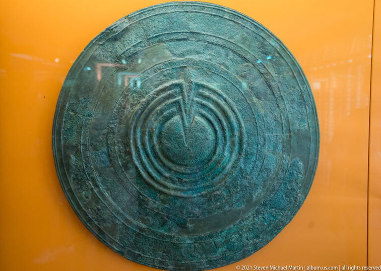 Round green-patinated bronze shield with concentric raised rings and geometric decoration.