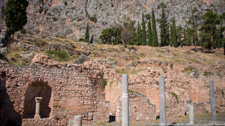 Reddish ancient masonry wall with a deep arched niche and several pale column shafts in front.