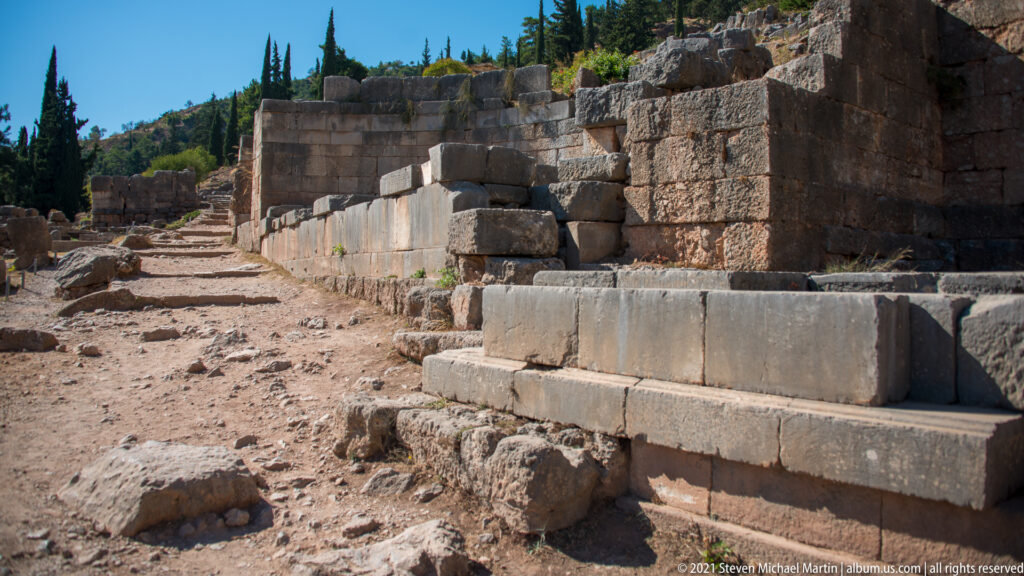 Ascending dirt-and-stone path beside massive dressed blocks and monument foundations at Delphi.
