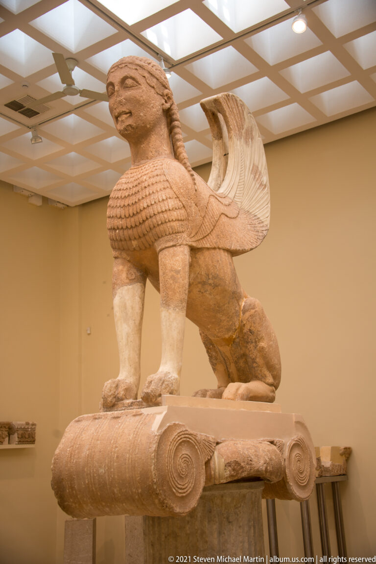 Archaic Sphinx of Naxos with female head, lion body, and raised wings standing on a large Ionic capital.