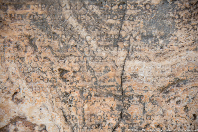 Close view of weathered Greek letters carved across a cracked and stained stone surface at Delphi.