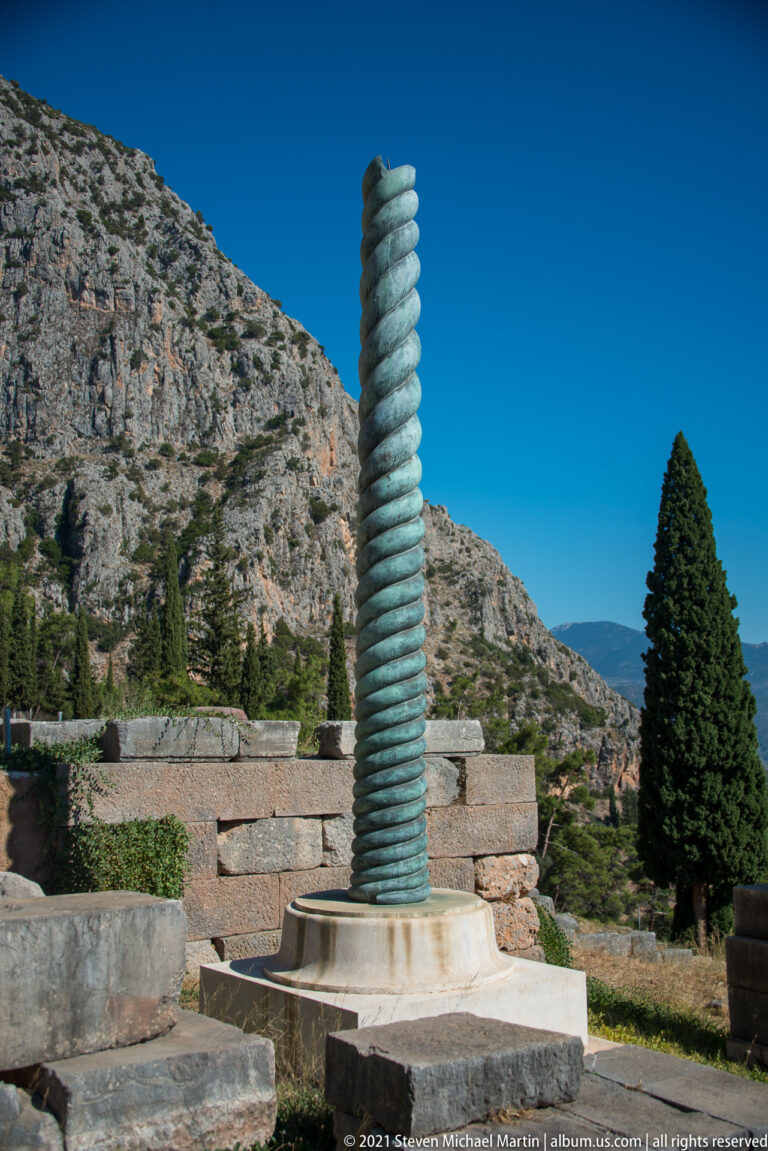 Greenish spiral reconstruction of the Serpent Column standing on a circular base within the Delphi sanctuary.