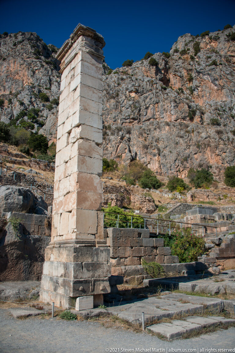 Tall rectangular ashlar stone pier standing beside ancient steps, with rocky cliffs rising behind.