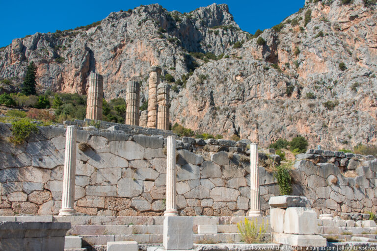 Standing ancient columns and stone terrace walls below the steep Phaedriades cliffs at Delphi.