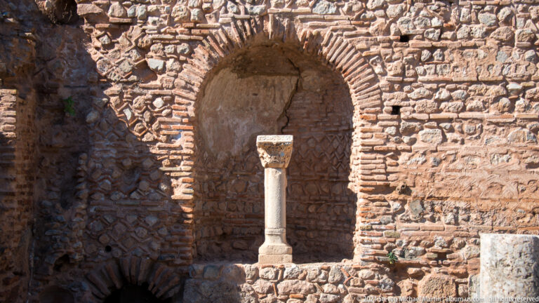 Arched brick-and-stone niche with a slender column standing inside the recess at Delphi.