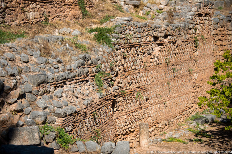 Long ancient wall combining irregular stones, small rubble masonry, and horizontal brick courses at Delphi.